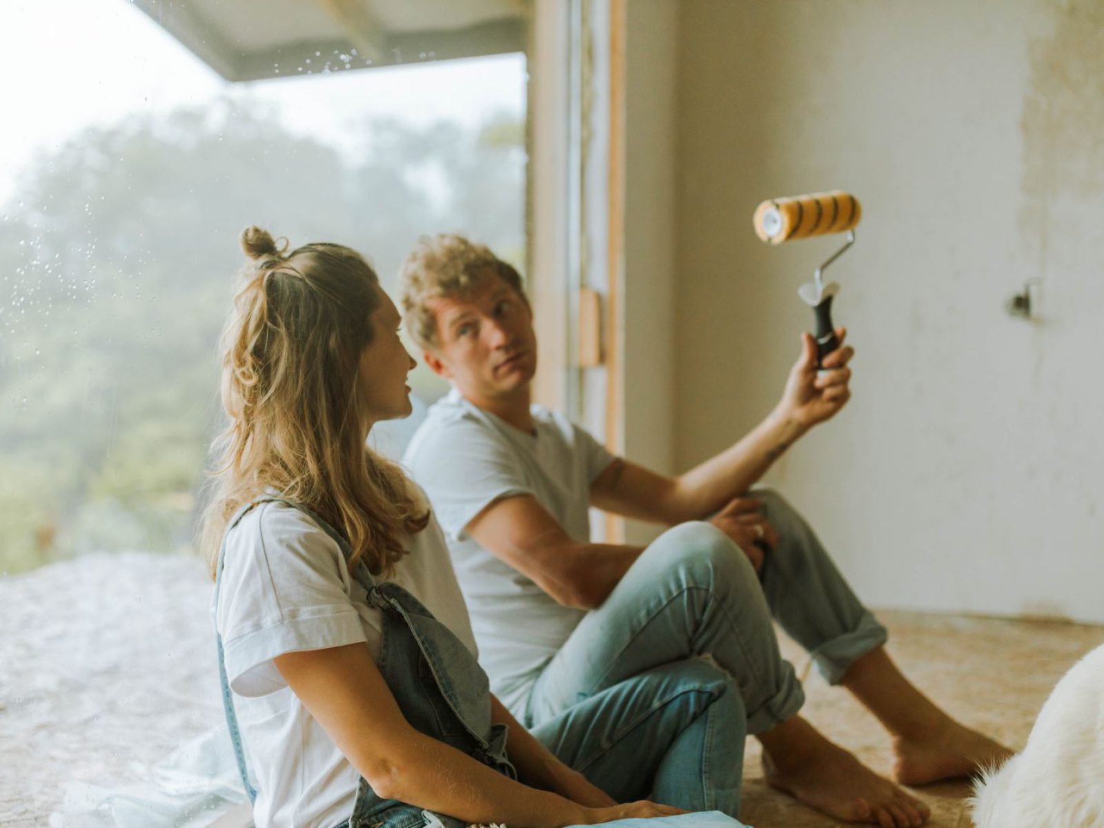 A young couple sits indoors planning their home renovation with a paint roller.